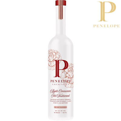 A white Penelope Bourbon bottle with floral designs and a large gold “P” displays the label “Penelope Apple Cinnamon Old Fashioned Ready-to-Pour Bourbon Cocktail,” made with whiskey, maple syrup, and bitters. The Penelope logo is in the top right corner.